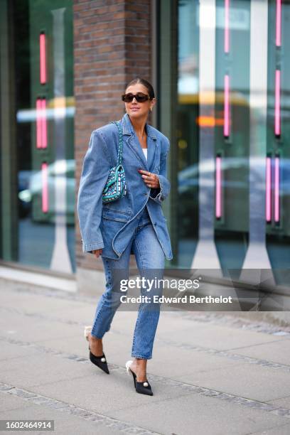 Darja Barannik wears brown marble sunglasses from Celine, gold earrings, a blue denim oversized blazer jacket, matching blue denim large pants, a...