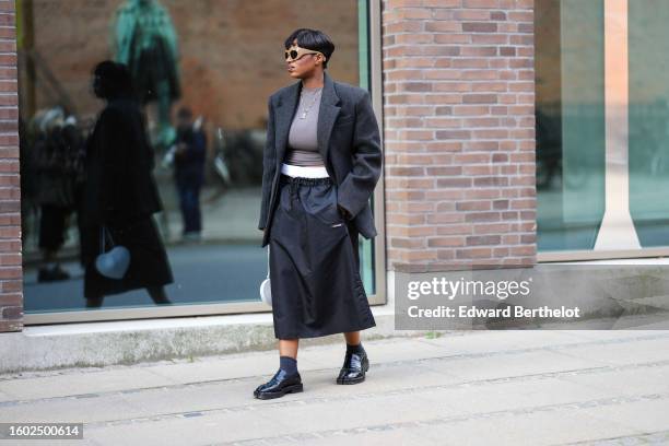 Loicka Grace wears beige large puffy sunglasses, a gray t-shirt, a gray oversized blazer jacket, a matching dark gray midi skirt from Lovechild, a...