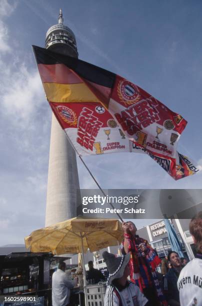 The Olympiaturm rising beyond Bayern fans waving a flag outside the Olympiastadion in Munich, Bavaria, Germany, 26th February 2000. The fans are...