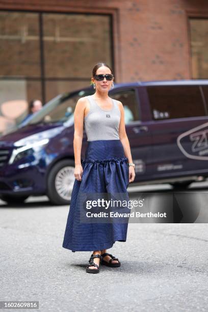 Idalia Salsamendi wears black sunglasses, gold earrings, a pale gray tank-top from Loewe, a navy blue denim high waist long skirt, a silver watch,...