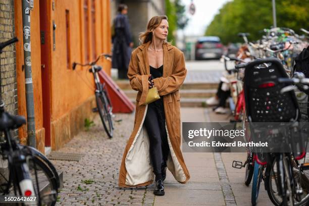 Guest wears silver earrings, a silver necklace, a black V-neck silk / satin long skirt, a dark brown suede long coat, black shiny varnished leather...