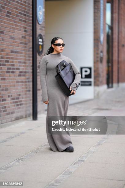 Guest wears black squared sunglasses, a gray wool high neck / long sleeves / long dress, a black shiny leather oversized squared handbag from...