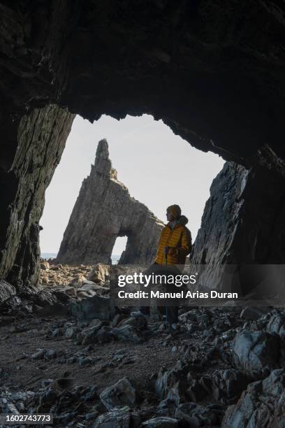 boy in yellow coat and cap getting to know the coast of asturias in spain. discovering a cave in a cliff after low tide. - one teenage boy only fotografías e imágenes de stock