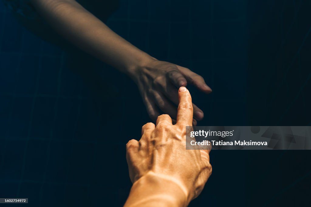 A woman's hand touches another hand underwater. The concept of life and death, a living person and artificial intelligence.