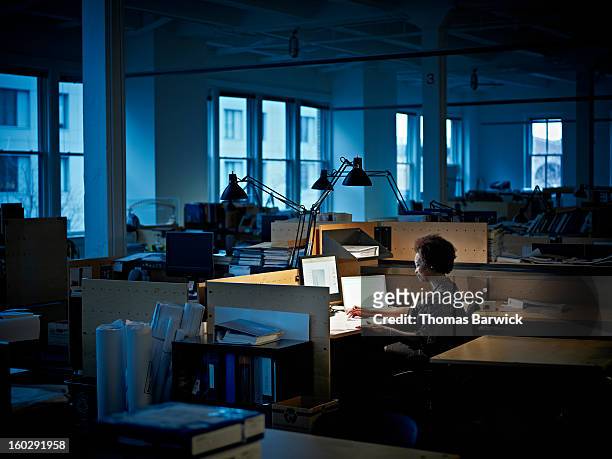businesswoman examining documents at desk at night - solitario foto e immagini stock