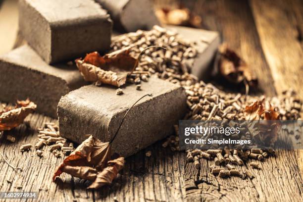 a pile of wood heating briquettes and pellets on a worn board somewhere in an old boiler room. - pellet foto e immagini stock