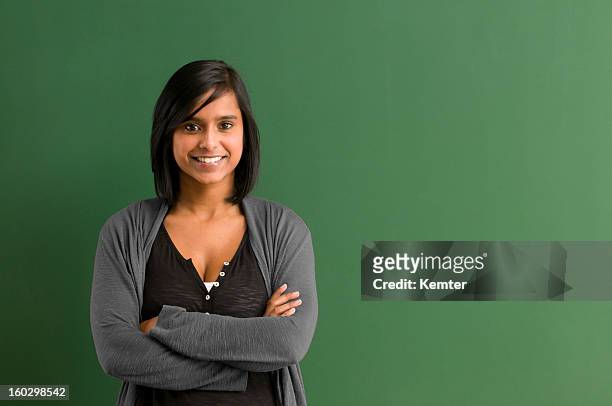 smiling teacher with arms folded in front of blackboard - green background stock pictures, royalty-free photos & images