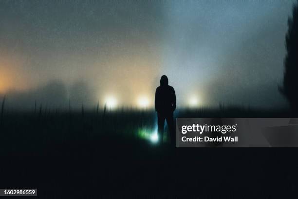 an abstract blurry grainy edit of a spooky hooded figure silhouetted on a foggy night in a field. with a dark, eerie atmosphere. - capucha fotografías e imágenes de stock