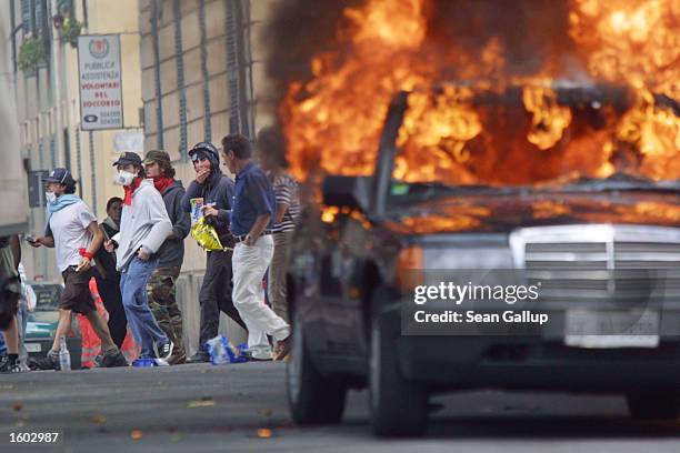 Anti-G8 protesters make their way past a car set alite by other protesters July 20, 2001 in central Genoa. Approximately 600 violent protesters...