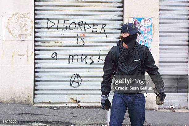 An anti-G8 protester carrying pavement stones passes a graffitied storefront July 20, 2001 in central Genoa. Approximately 600 violent protesters...