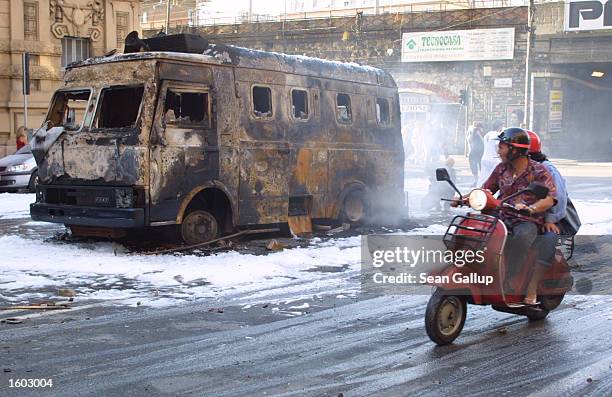 People on a moped pass the burnt remains of a police van set afire by anti-G8 protesters July 20, 2001 in central Genoa. Approximately 600 violent...