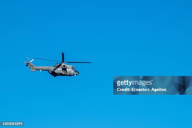 spanish air force search and rescue helicopter (as332 super puma) flying against a clear sky with two crew members sitting in the door looking at camera - spanish military - fotografias e filmes do acervo