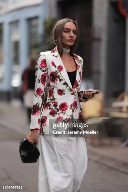 Guest is seen wearing silver rhinestones choker necklace, black cotton tank top, white with red roses print pattern blazer jacket, white wide leg...