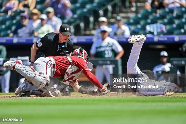 Jurickson Profar of the Colorado Rockies slides safely across home plate ahead of the tag attempt by Jose Herrera of the Arizona Diamondbacks in the...