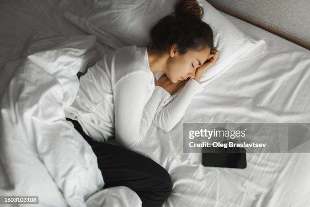 sad woman lying in bed with mobile phone and waiting for message. relationship difficulties, broken heart - woman sleeping stock pictures, royalty-free photos & images