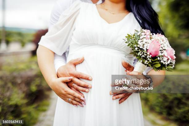 pregnant bride holds flowers while husband holds her belly - belly ring 個照片及圖片檔