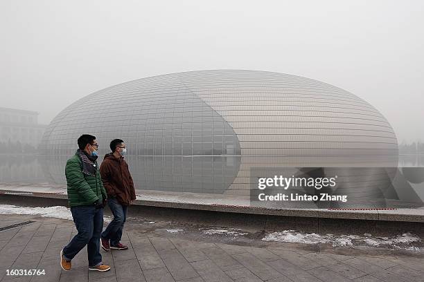 Beijing residents wearing masks walk in front of a fog-shrouded National Grand Theater as severe pollution continues to affect the capital on January...