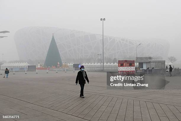 Woman wearing a mask walks across a square in front of a fog-shrouded National Stadium as severe pollution continues to affect the capital on January...