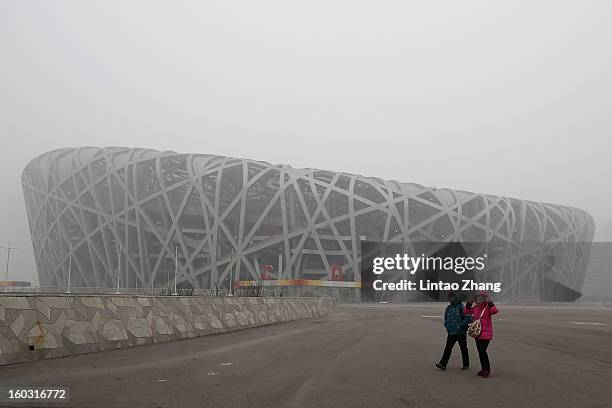 Beijing residents wearing masks walk in front of a fog-shrouded National Stadium as severe pollution continues to affect the capital on January 29,...