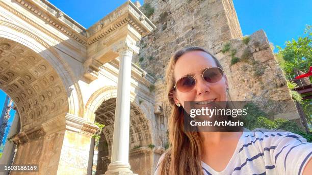 woman makes selfie while traveling in the old city of antalya, turkey and exploring the famous sightseeing hadrian's arch - art of the vintage selfie stockfoto's en -beelden