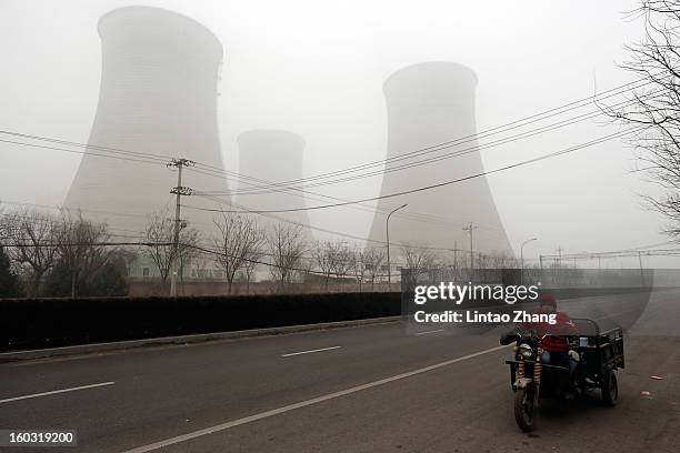 Men rides a three-wheeled motorcycle on the street through power station chimney during severe pollution on January 29, 2013 in Beijing, China. The...