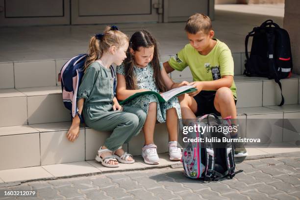 group of small school kids sitting with satchels on stairs doing homework - summer camp stock-fotos und bilder