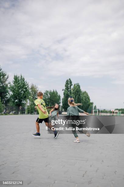 three school children in casual clothes running and having fun together on paved yard - fangen stock-fotos und bilder