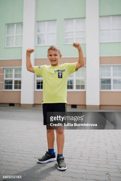 portrait of small blond boy standing with raised hands in front of school building - boyshorts fotografías e imágenes de stock