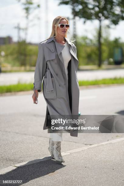 Guest wears white and orange sunglasses from Louis Vuitton, gold earrings, a gold micro chain necklace, a white long tube dress, a pale gray belted...