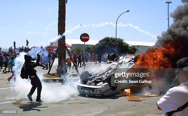 An anti-G8 protester throws a tear gas canister back at police while a car burns nearby during street fighting July 21, 2001 in Genoa, Italy. Several...