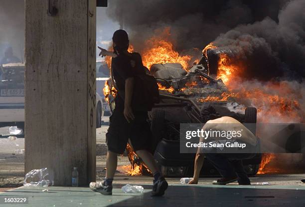 Anti-G8 protesters hide behind a burning car as they fight police July 21, 2001 in Genoa, Italy. Several thousand violent protesters battled with...