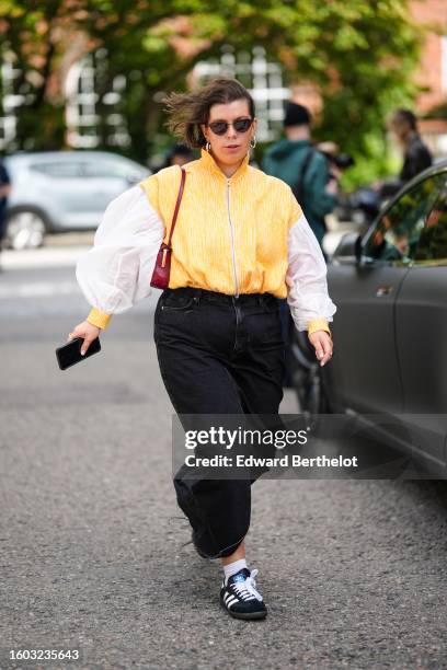 Guest wears black sunglasses, silver earrings, a yellow and white striped print pattern polar zipper wool pullover with white tulle long puffy...