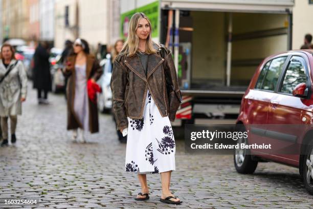 Guest wears a gray wool pullover, a dark brown faded denim oversized leather jacket, a white with embroidered black flower pattern midi dress, black...