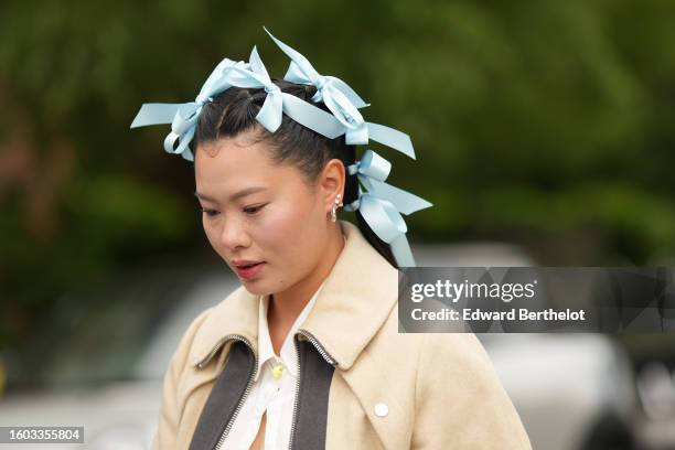 Guest wears a pale blue ribbons on the hair, a white shirt, a beige with black print pattern zipper jacket, outside Stamm, during the Copenhagen...