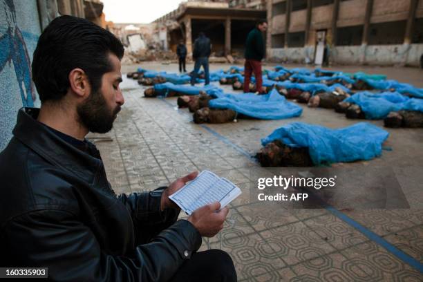 Man reads the Koran next to the bodies of Syrian civilians executed and dumped in the Quweiq river, in the grounds of the courtyard of a Yarmouk...