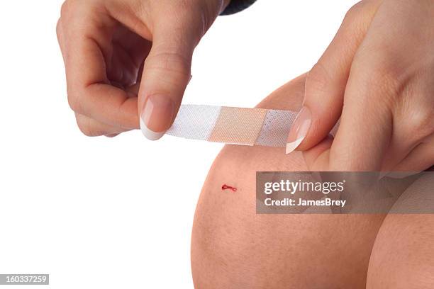 first aid; applying bandage to cut knee - applying plaster stock pictures, royalty-free photos & images