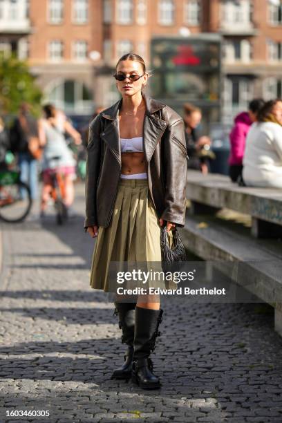 Guest wears black sunglasses, gold earrings, a gold micro chain necklace, a dark brown faded leather oversized zipper jacket, a white shoulder-off...