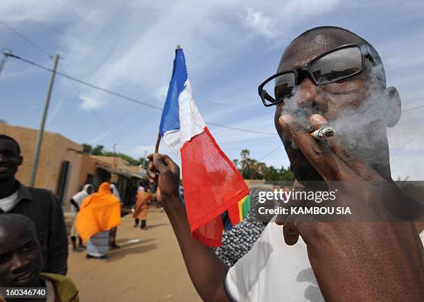French flag is seen next to a man enjoying a cigarette on January 29, 2013 in Ansongo, a town south of the northern Malian city of Gao, as Niger...