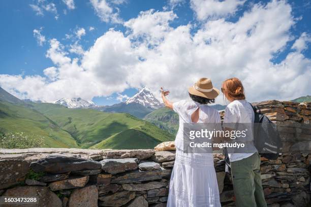 deux amies femele regardant la vue sur les montagnes du caucase à kazbegi en géorgie - montagnes du caucase photos et images de collection
