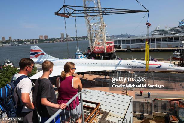 People watch as the British Airways Concorde is seen lifted on a crane at the Intrepid Museum on August 09, 2023 in New York City. The British...