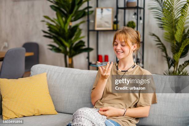 woman sending a voice message while relaxing at home - mike glad stockfoto's en -beelden