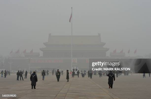 People walk on Tiananmen Square in front of Tiananmen Gate with the portrait of Mao Zedong during heavy air pollution in Beijing on January 30, 2013....