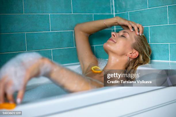 charming blond woman relaxes in divine bubble bath with aromatic citrus slices - woman bath tub wet hair stock pictures, royalty-free photos & images