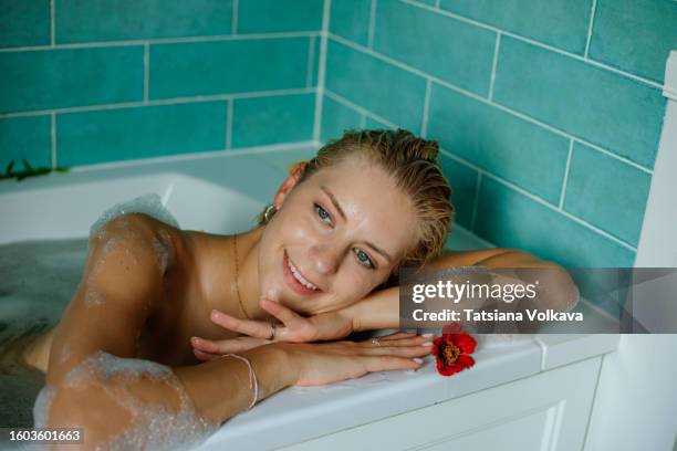 cheerful blond woman with alluring smile lying in bubble bath contemplating about exciting trip to tropical resort - woman bath tub wet hair stock pictures, royalty-free photos & images