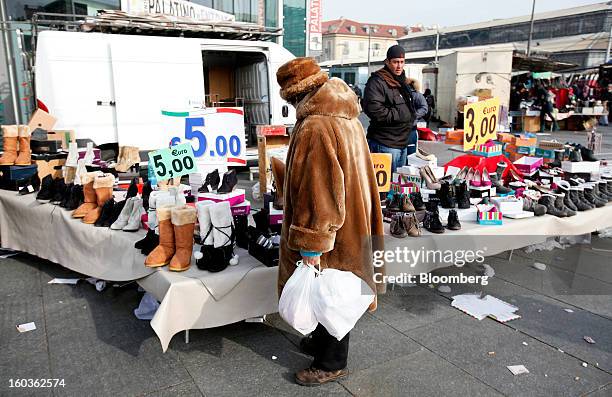 Pedestrian holds shopping bags as she browses shoes displayed for sale on a street market stall in Turin, Italy, on Tuesday, Jan. 29, 2013. Italy...