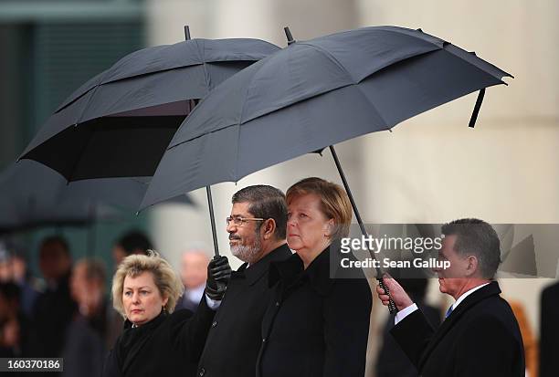 German Chancellor Angela Merkel and Egyptian President Mohamed Mursi listen to their countries' respective national anthems under pouring rain upon...