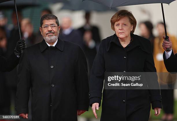 German Chancellor Angela Merkel and Egyptian President Mohamed Mursi review a guard of honour under pouring rain upon Mursi's arrival at the...