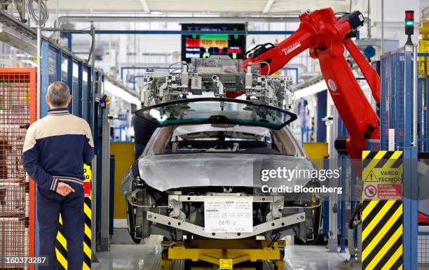 An employee watches as a Comau SpA robot positions a windscreen over the bodyshell of a Maserati Quattroporte luxury automobile during production at...