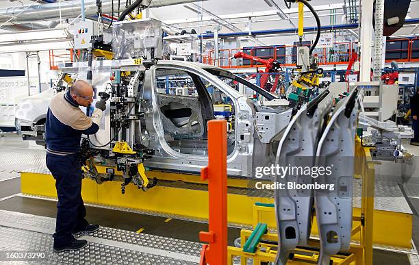 An employee uses a robot as he mounts a rear passenger door onto the bodyshell of a Maserati Quattroporte luxury automobile as it travels along the...