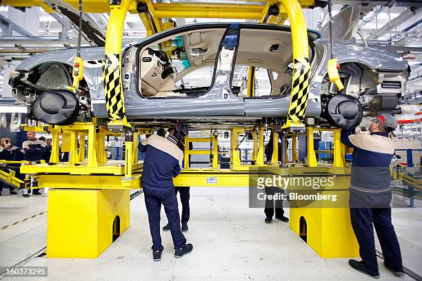 Employees work beneath a Maserati Quattroporte luxury automobile as it travels along the production line at Fiat SpA's Grugliasco factory in Turin,...